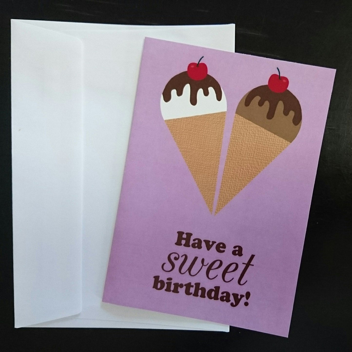 Greeting card with ice cream cones and 'Have a sweet birthday!' text on a purple background