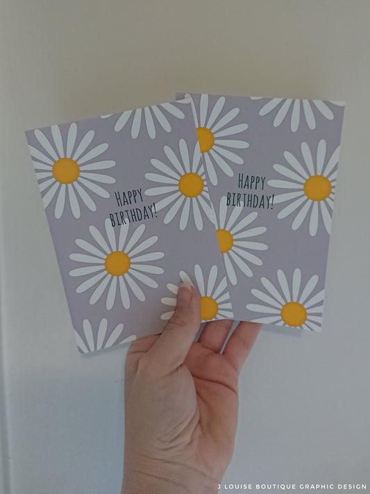 Two birthday cards with daisy designs held by a hand against a white background.